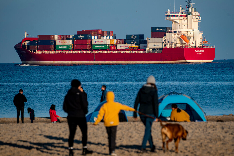 Strandspaziergänger schauen auf einen Containerfrachter. (Symbolbild)