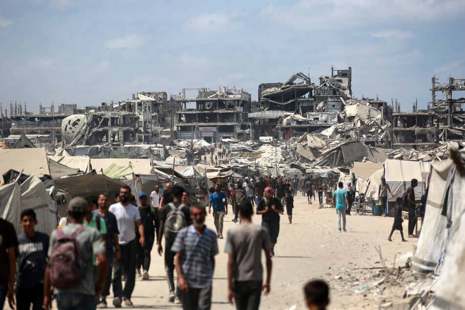 Palestinians walk along a street near buildings destroyed by Israeli bombs in Gaza City on August 8, 2025.