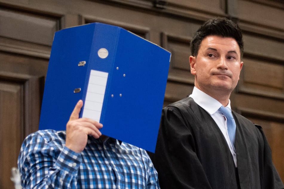 Der Angeklagte (links) verbirgt zu Prozessbeginn sein Gesicht hinter einem Aktenordner, er steht neben seinem Verteidiger Haydar Güler. (Archivbild)
