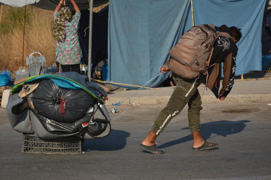 Ein Migrant trägt einen Rucksack und zieht seine Habseligkeiten hinter sich her.