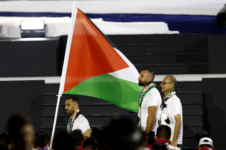 Fadi Aldeeb (l.) raises his country's flag as he prepares to compete in shot put at the Paris Paralympics.