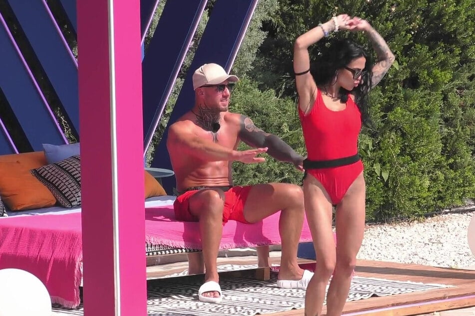 Elena tanzt ausgelassen bei der Baywatch-Session, im Hintergrund sitzt der mutmaßlich vergebene Johannes.