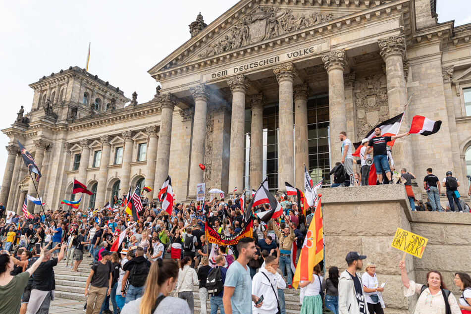 Teilnehmer einer Kundgebung gegen die Corona-Maßnahmen stehen am Samstag auf den Stufen zum Reichstagsgebäude, zahlreiche Reichsflaggen sind zu sehen.