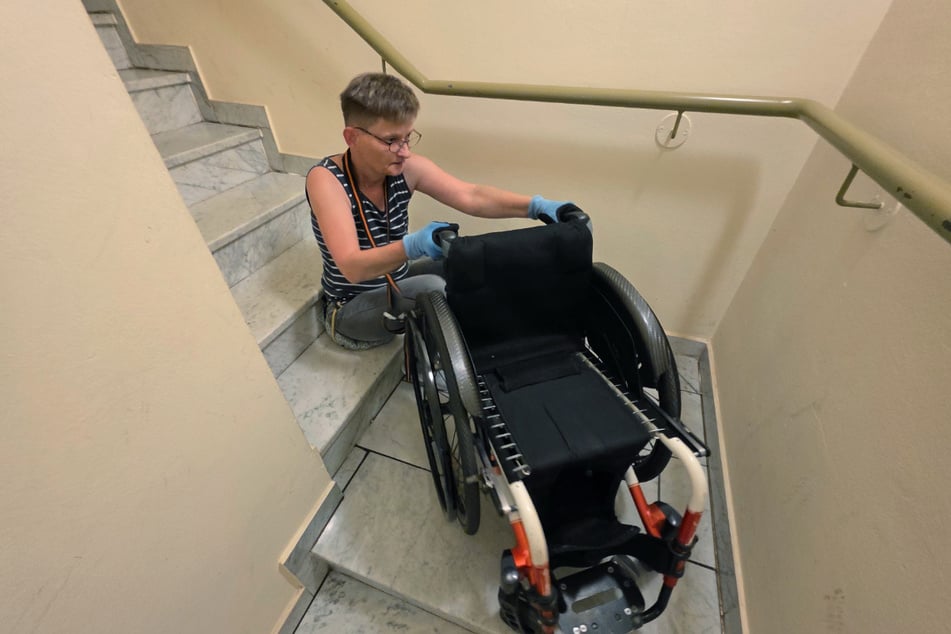 Heike Z. quält sich die Treppen hoch, den Rollstuhl hat sie an ihrem Nacken mit einem Gurt befestigt ...