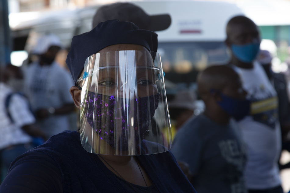 Südafrika, Johannesburg: Eine Frau, die eine Schutzbrille, einen Mund-Nasen-Schutz und ein Gesichtsvisier trägt, steht vor dem Hauptbahnhof.