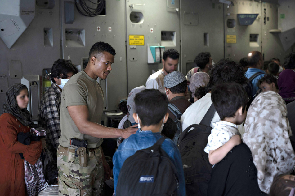 A US Airman assists Afghan refugees board an Air Force aircraft during an evacuation from Hamid Karzai International Airport on August 24, 2021, in Kabul, Afghanistan.