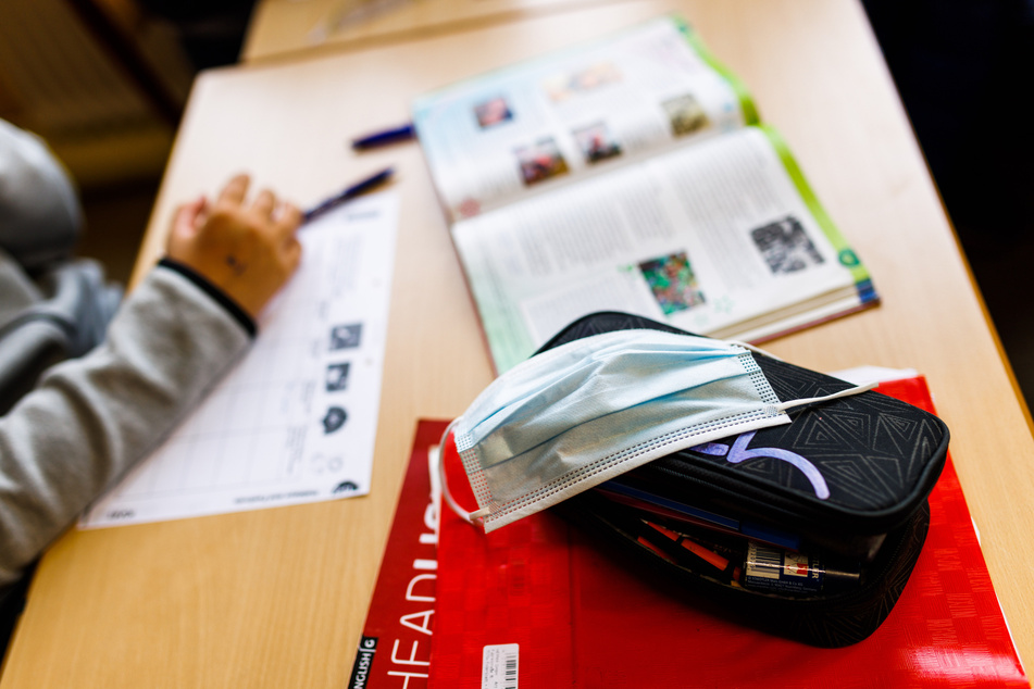 Eine Mund-und-Nasen-Schutzmaske liegt neben einem Schulbuch auf einem Tisch in einer Schule.