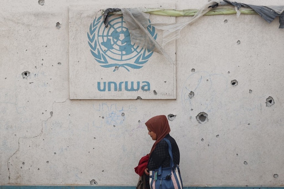 A Palestinian woman walks past a damaged wall bearing the UNRWA logo at a camp for internally displaced people in Rafah in the southern Gaza Strip.