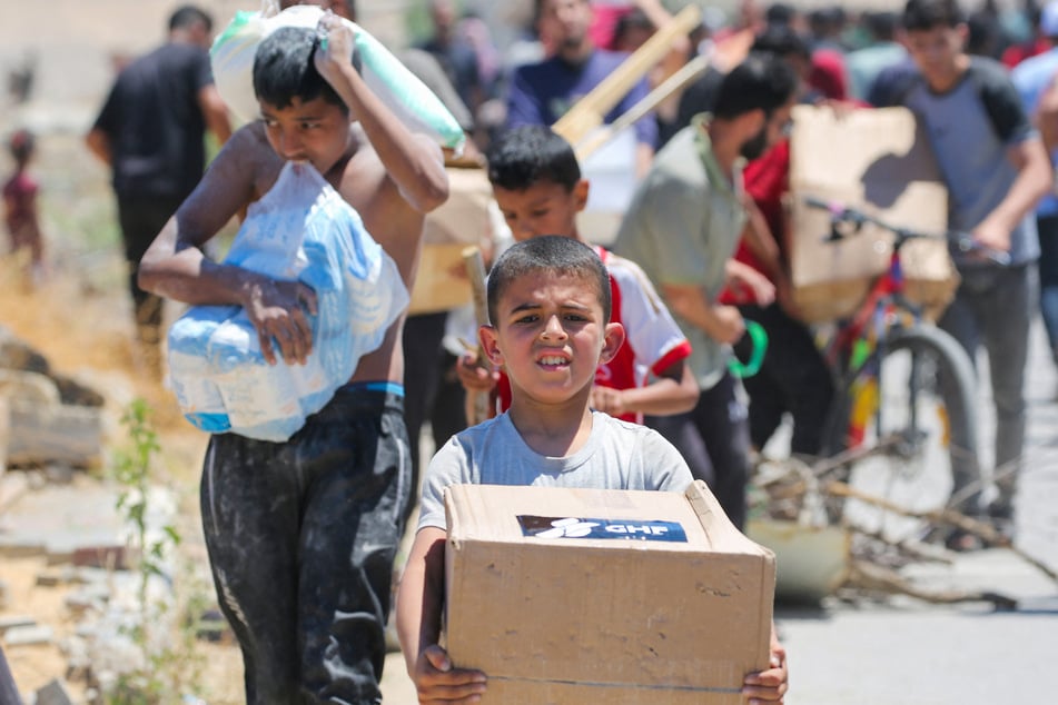 A boy carries a box of relief supplies from the Gaza Humanitarian Foundation as displaced Palestinians return from an aid distribution center in the central Gaza Strip.