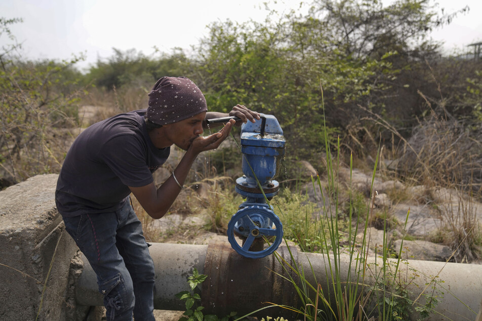 Ein Mann trinkt am Rande von Hyderabad in Indien Wasser aus einer undichten Wasserstelle.