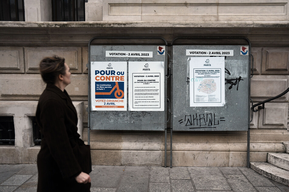 Eine Frau geht an einem Plakat vorbei, auf denen die Bürger zur Abstimmung über die Zukunft der Miet-E-Scooter in der Stadt aufgerufen wird. Bald geht es auch um die SUV-Zukunft in Paris.