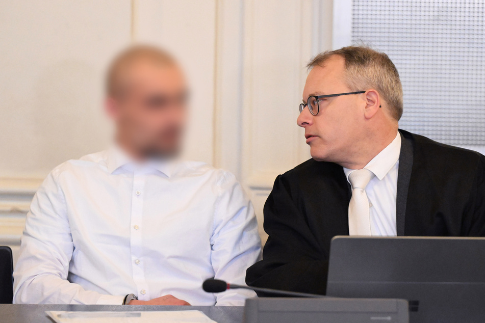Der Angeklagte (21, l.) im Prozess zu einer mutmaßlichen Geiselnahme wartet im Schwurgerichtssaal des Landgerichts Karlsruhe zusammen mit seinem Anwalt Alexander Kist auf den Prozessbeginn.