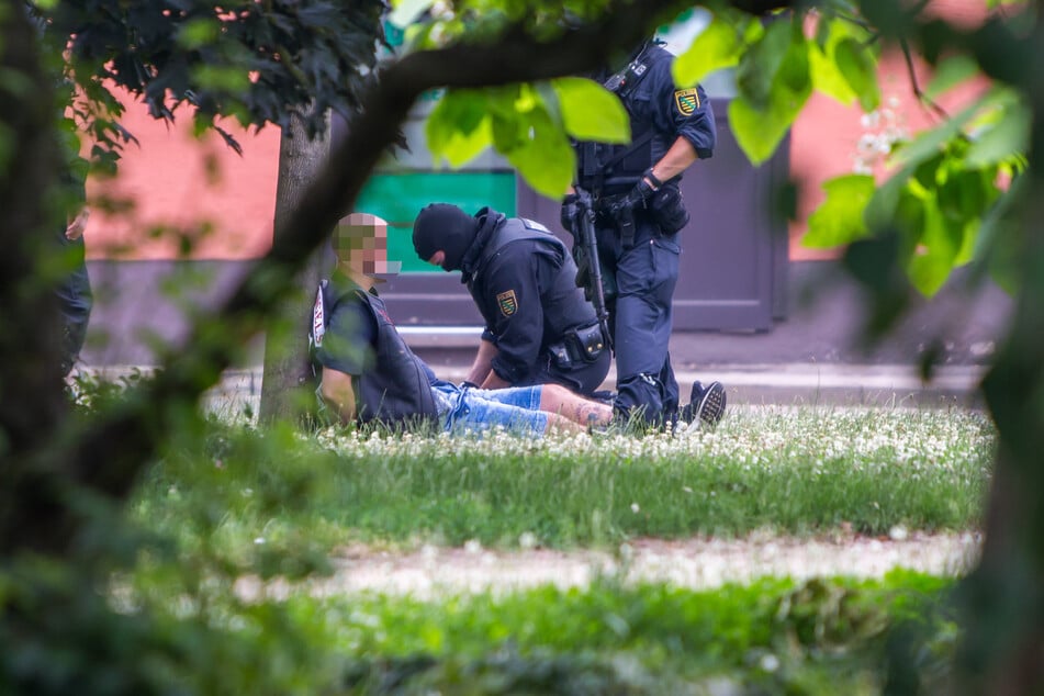 Vermummte Polizisten durchsuchen einen an den Händen gefesselten Rocker am Tatort.