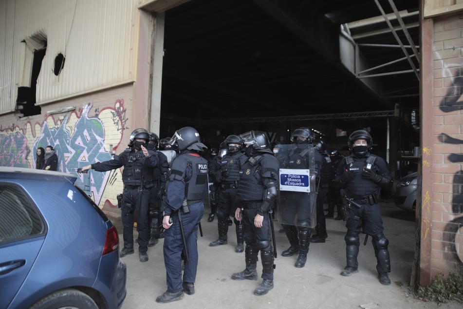 Llinars del Vallès: Polizeibeamte der Mossos d'Esquadra stehen in schwerer Montur vor einer Lagerhalle, um dort eine Rave aufzulösen.
