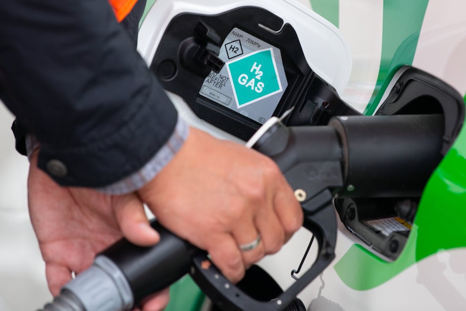 Ein Mann steckt ein Zapf-Ventil von einer Wasserstoff-Tankstelle in den Tankstutzen eines Wasserstoffautos. (Symbolbild)