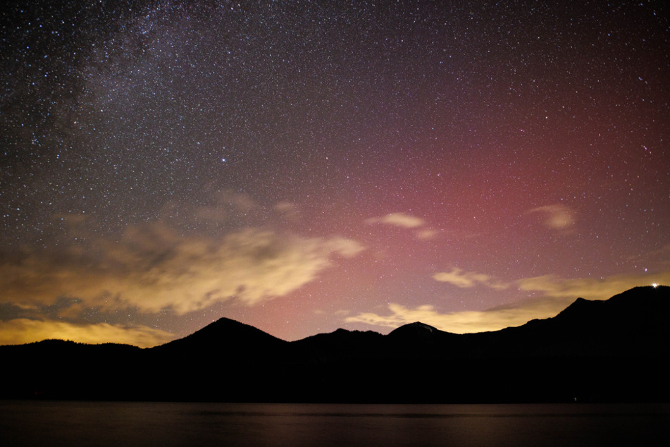 Polarlichter schimmern am Sternenhimmel über den Bergen am Walchensee.