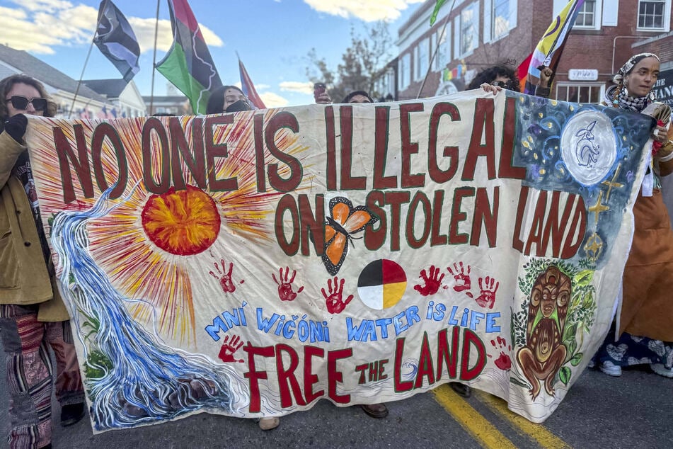 People raise a banner reading "No One Is Illegal on Stolen Land" during the 2025 National Day of Mourning.