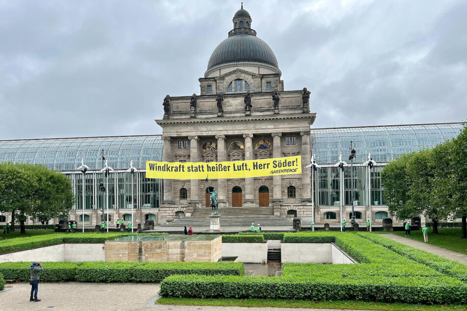 Umweltaktivisten von Greenpeace haben vor der Staatskanzlei in München an sechs Fahnenmasten Windräder befestigt und richten sich mit einem Banner direkt an den Ministerpräsidenten.