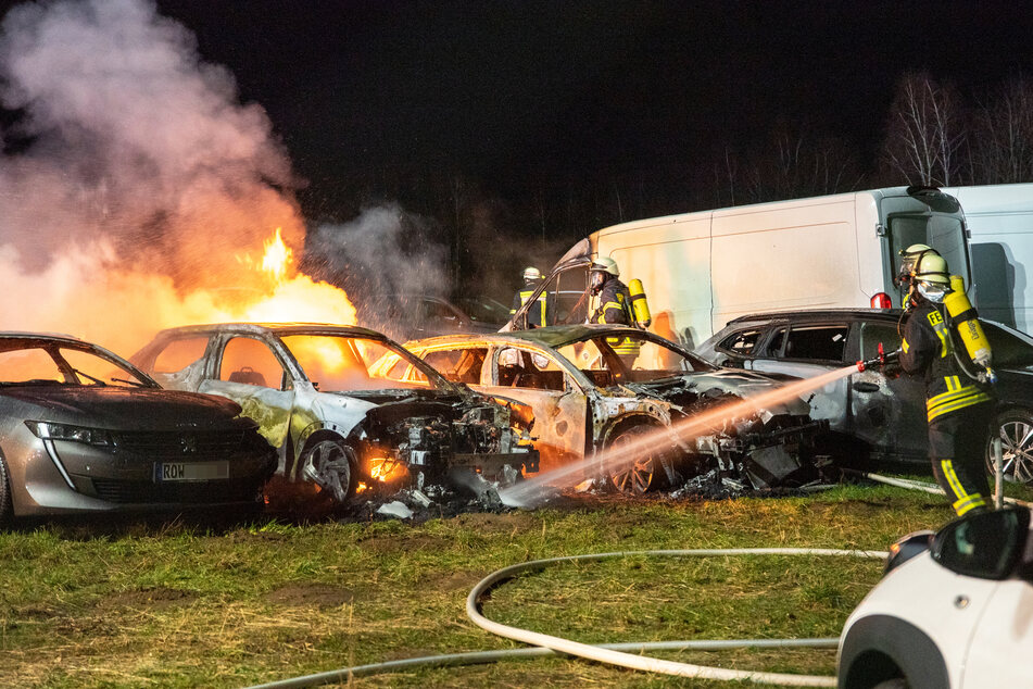 Feuerwehrleute löschen die brennenden Autos.