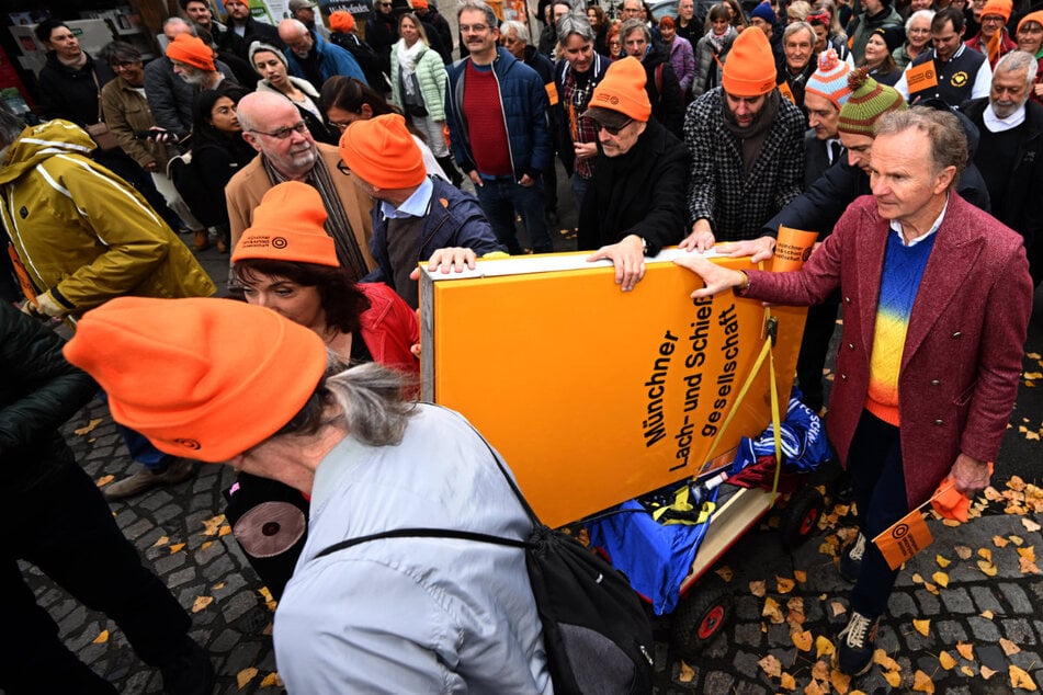 Das Schild der Lach- und Schießgesellschaft wird von den Mitgliedern auf einem Leiterwagen zur U-Bahn gefahren.