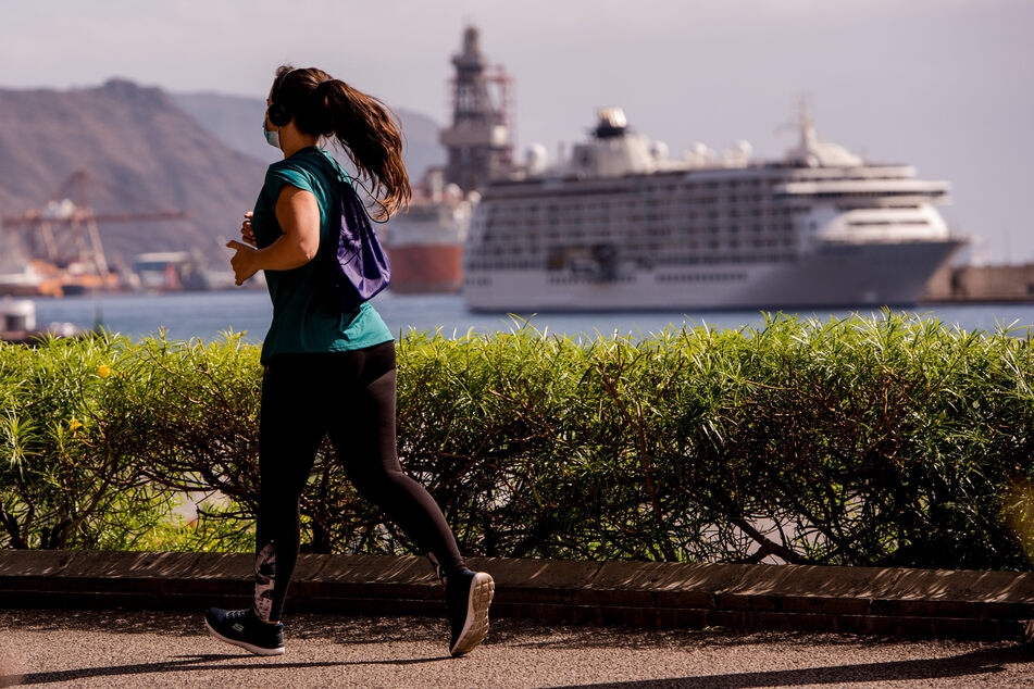Eine Frau joggt, während im Hintergrund ein Kreuzfahrtschiff im Hafen von Santa Cruz zu sehen ist.