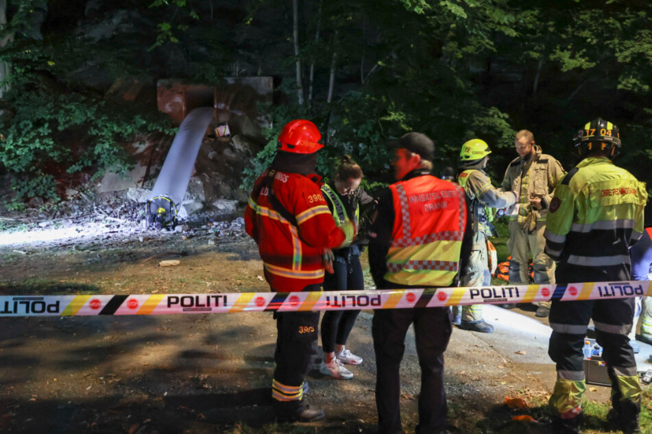 Rescue workers stand together in a cordoned off area.  After a party in an underground bunker in Norway, 25 people were taken to hospitals with suspected carbon monoxide poisoning.