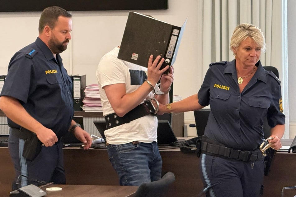 Der 39-Jährige (M.) wird von Polizisten im Landgericht Memmingen auf die Anklagebank geführt.
