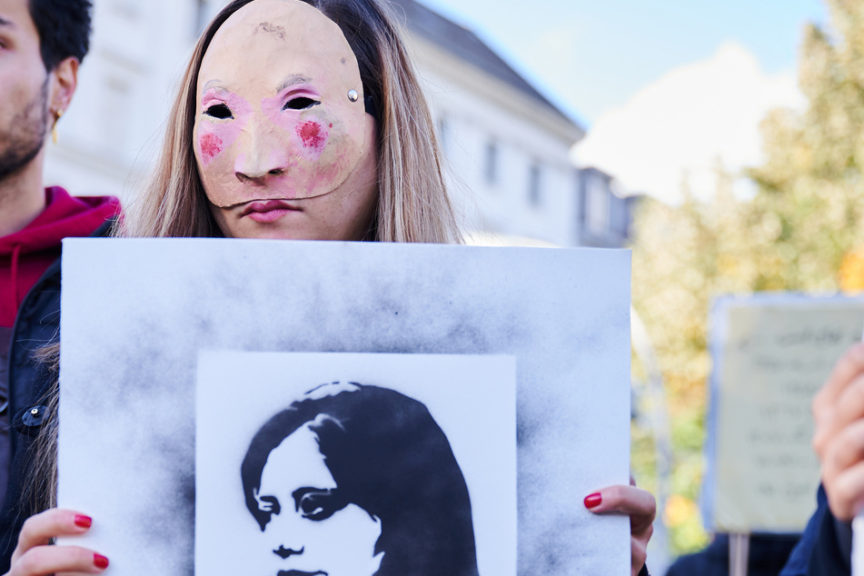 Eine maskierte Frau hält ein Bild von Mahsa Amini (✝22) hoch und protestiert gegen die Frauengewalt im Iran.