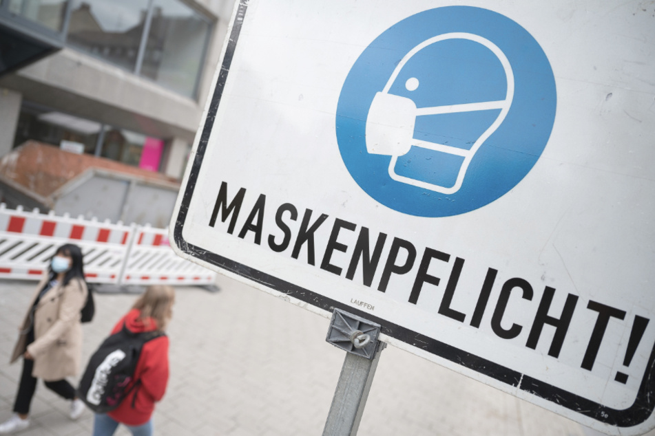 Zwei Passantinnen gehen in einer Fußgängerzone hinter einem Schild vorbei, auf dem "Maskenpflicht" steht.