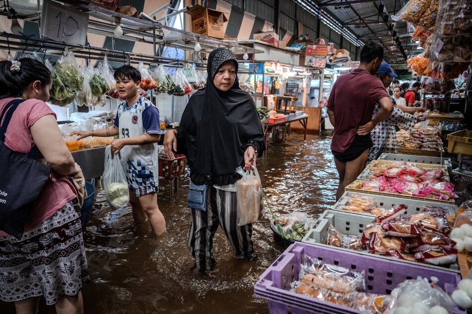 Menschen kaufen Lebensmittel auf einem überfluteten Frischmarkt in Bangkok.