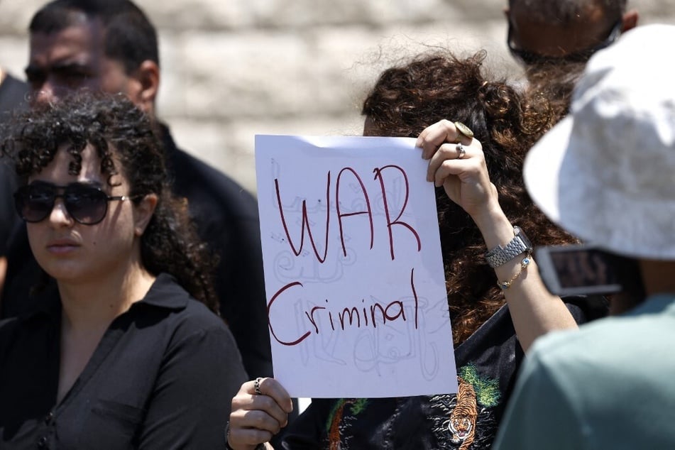 A woman holds a sign reading "War Criminal" as she and others demonstrate against Israeli Prime Minister Benjamin Netanyahu during his visit to the Druze village of Majdal Shams.