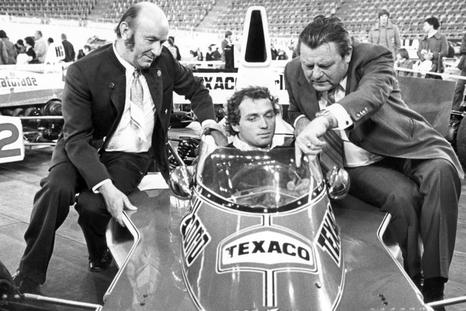 Jochen Mass (M.) erklärte im November 1975 dem damaligen CSU-Chef Franz Josef Strauß (r.) einen McLaren M 23 bei der "Greger-Racing-Show" in München.