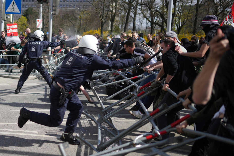 Wien: Demonstranten versuchen Straßenabsperrungen zu durchbrechen, hinter der zwei Polizisten stehen.