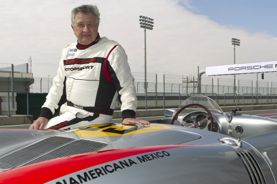 Rennfahrer-Legende Hans Herrmann posiert hier mit mehr als 90 Jahren vor einem schicken und schnellen Rennwagen.