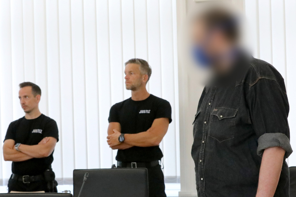 Der Angeklagte wartet neben Justizbeamten im Landgericht auf den Prozessauftakt.
