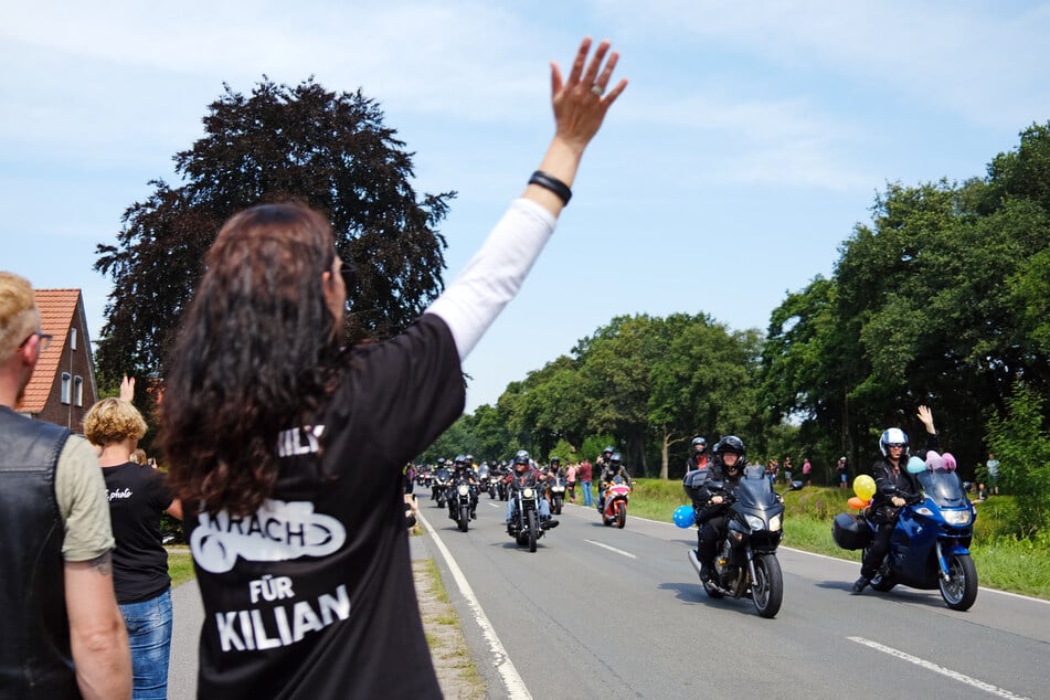 Eine Frau mit einem T-Shirt mit der Aufschrift "Krach für Kilian" winkt den Motorradfahrern, die am Haus des krebskranken Kilian vorbeifahren.