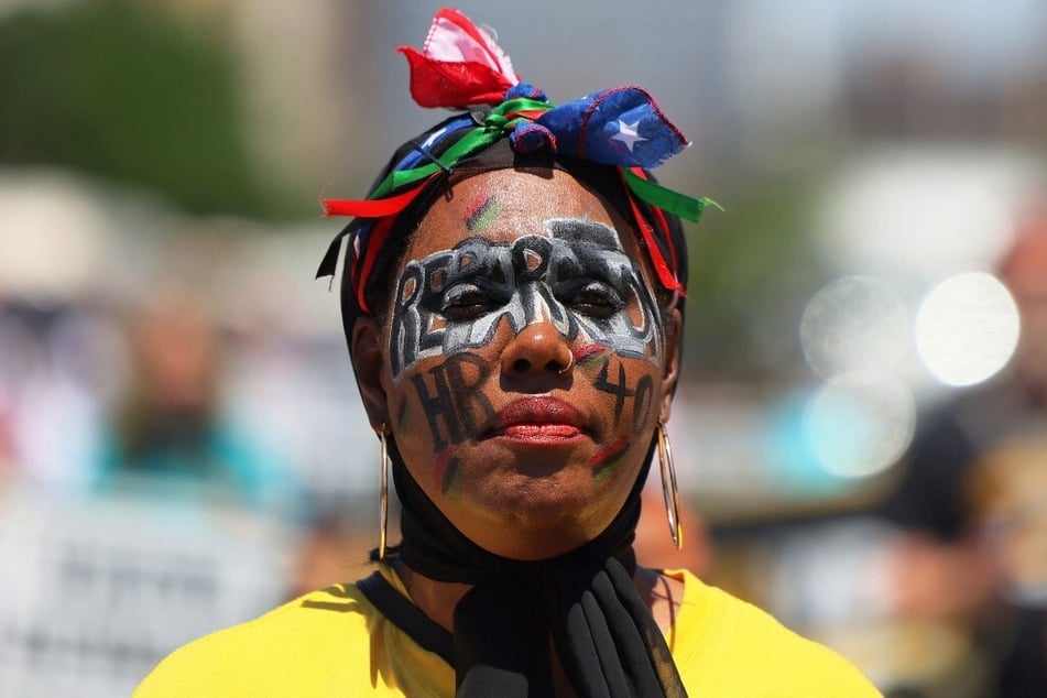 A New Jersey resident wears face paint reading "Reparations" and "HR 40" during a Juneteenth 2022 rally in Newark.