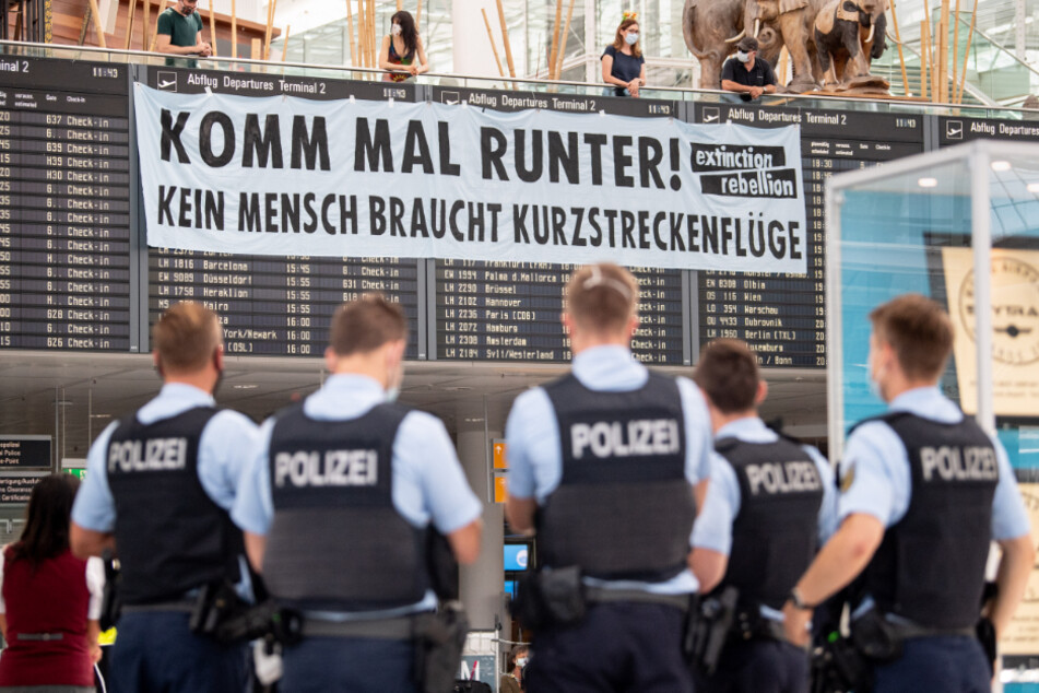 Polizisten stehen am Flughafen vor der Abflugtafel, über die Aktivisten der Gruppe "Extinction Rebellion" ein Banner gehängt haben.