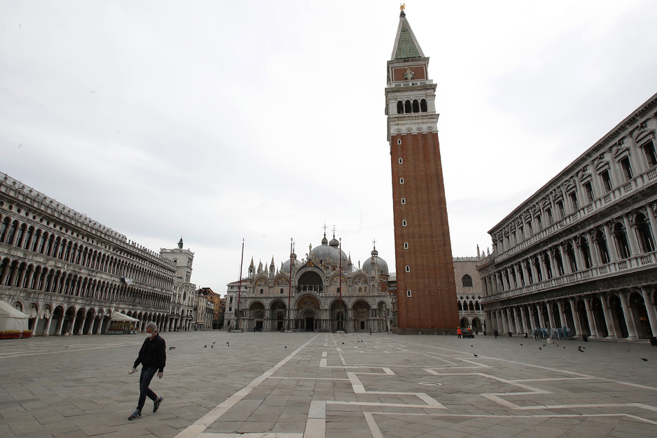 Italien, Venedig: Ein einzelner Mann mit einer Hygienemaske geht über den leeren Markusplatz. So haben die meisten Venezianer ihre Stadt wohl noch nie erlebt: keine Motorboote, keine Gondoliere und kaum Touristen. Selbst auf dem sonst überfüllten Markusplatz waren Selfies ohne Menschenmassen im Hintergrund möglich.