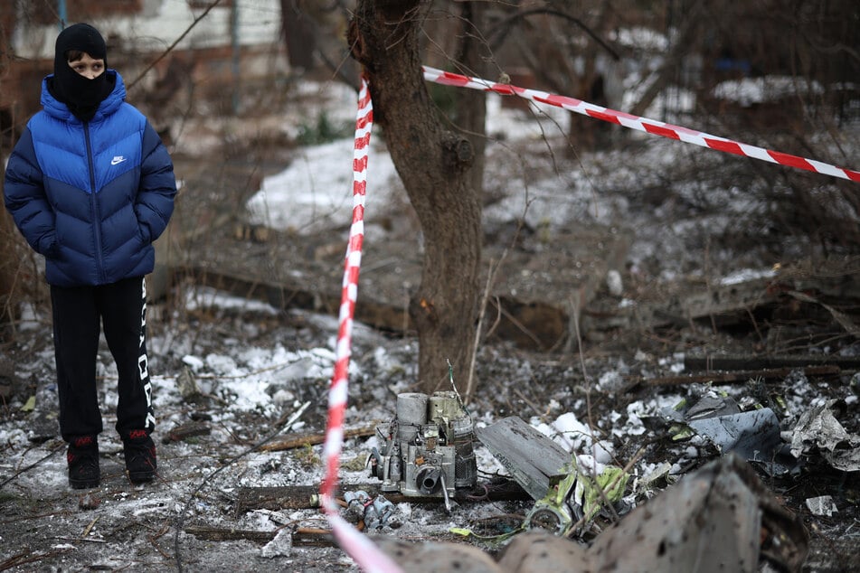 A child stands next to the remains of an airborne weapon at the site of a heavily damaged house following an air attack in Sofiivska Borshchagivka, Kyiv region, on February 22, 2026.