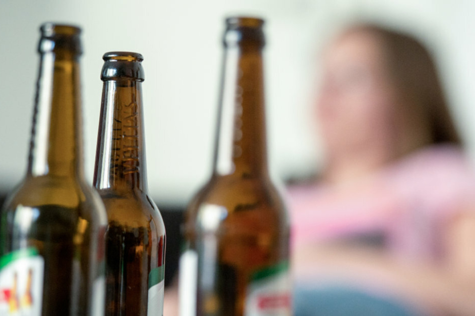 Eine junge Frau sitzt hinter leeren Bierflaschen (Symbolbild).