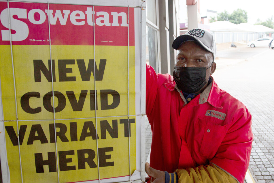 Ein Tankwart steht in Pretoria (Südafrika) neben einer Zeitungsschlagzeile mit dem Titel "New covid variant here" (dt. Neue Covid-Variante hier).