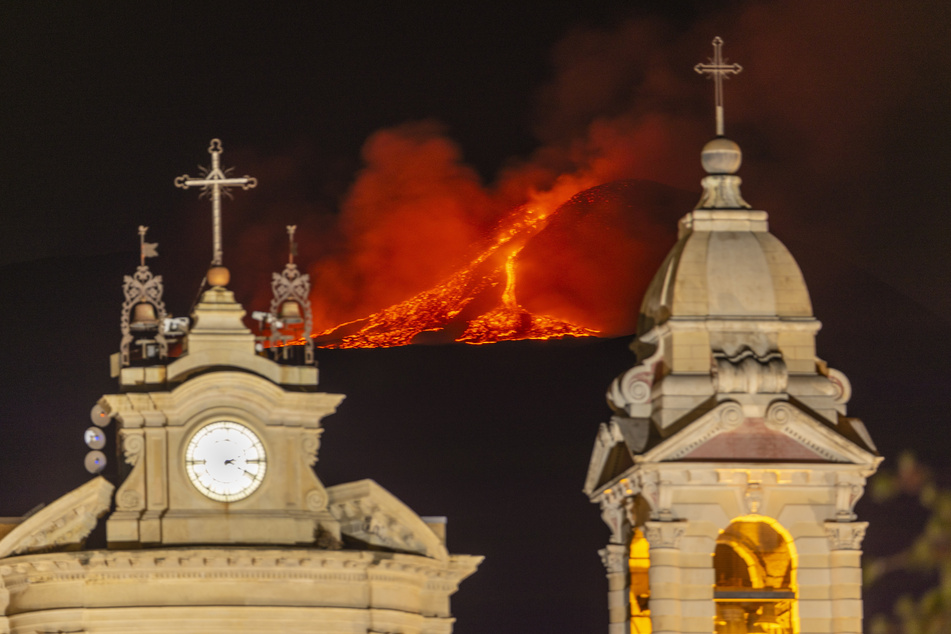 Lava bricht aus einem Krater des Ätna, Europas größtem aktiven Vulkan, hinter der Kirche Santa Maria della Guardia in Belpasso in der Nähe von Catania aus.