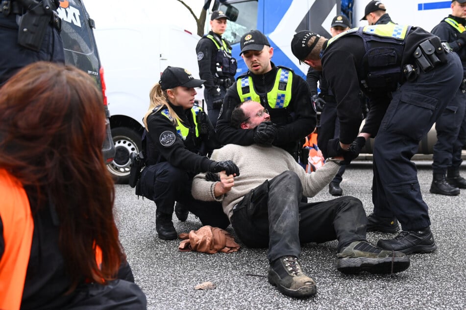 Polizisten halten einen Aktivisten fest, der sich auf der Fahrbahn festgeklebt hat.