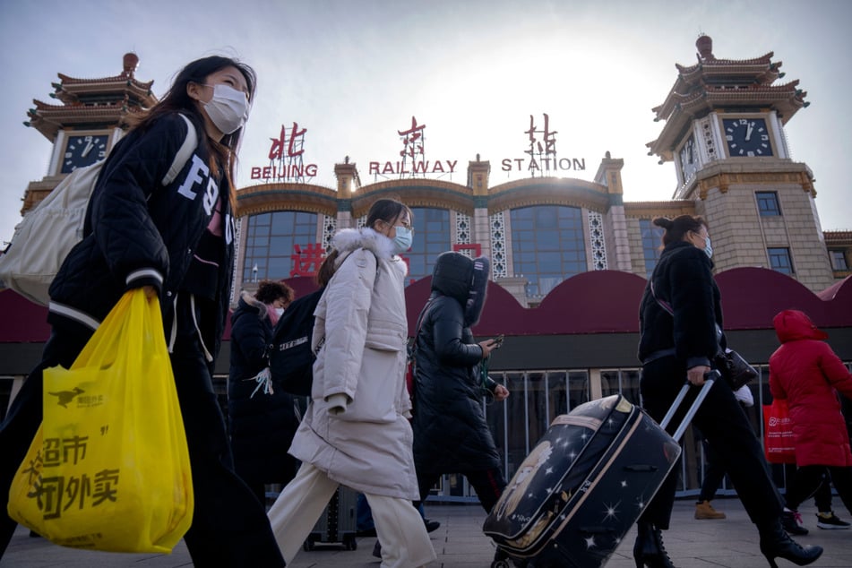 Reisende mit Mund-Nasen-Schutz gehen am Zentralbahnhof in Peking entlang.