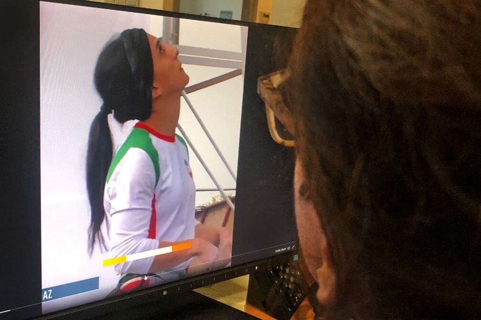 A woman looks at a screen displaying a video of an international climbing competition is Seoul, South Korea, during which Iranian climber Elnaz Rekabi competes without a hijab.