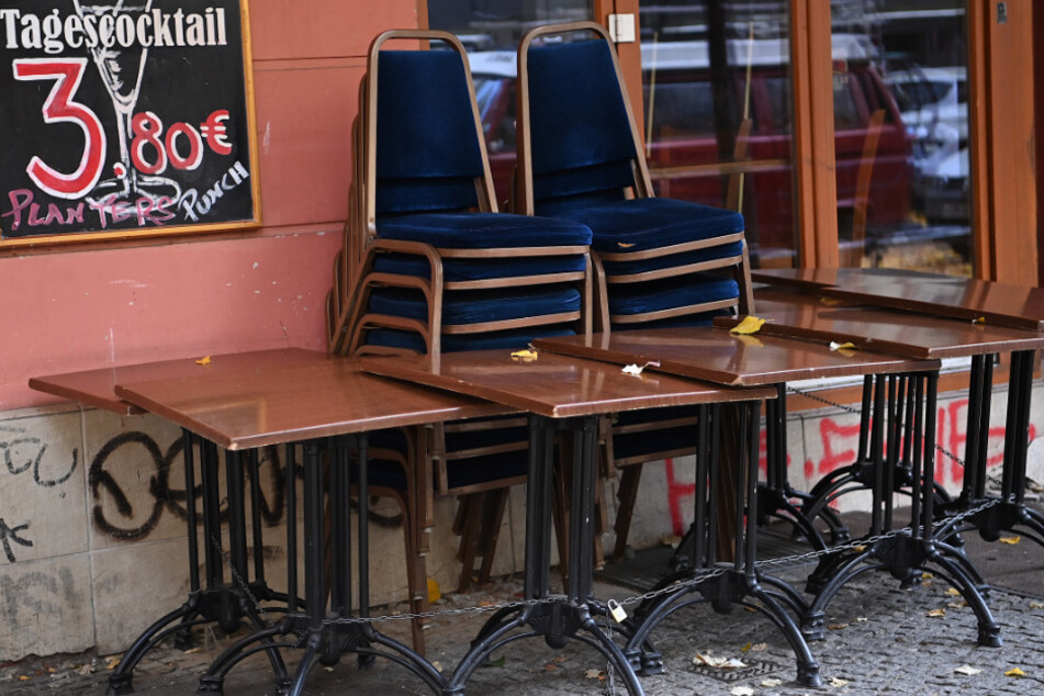 Stühle und Tische stehen zusammengestellt vor einer geschlossenen Bar.