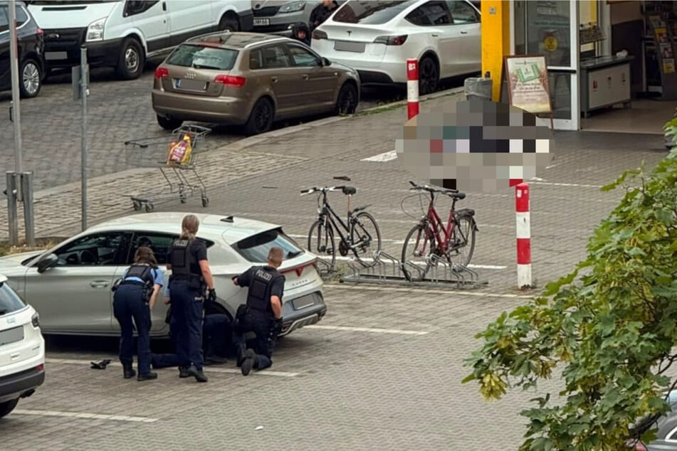 Polizisten suchen Deckung hinter einem geparkten Auto. Direkt vorm Netto-Eingang liegt der Tatverdächtige in seinem eigenen Blut.