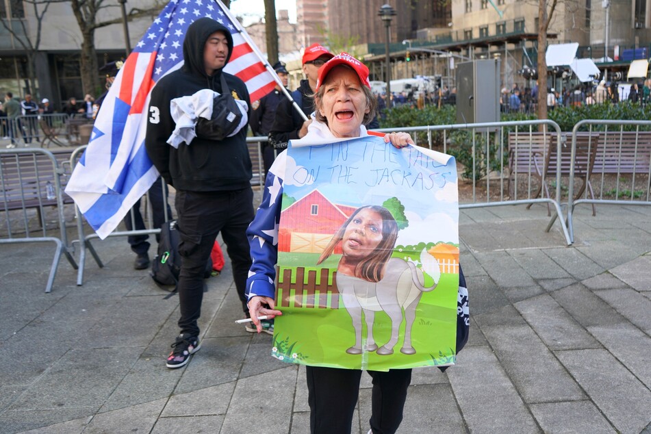 A Donald Trump supporter holds a sign that reads, "pin the tail on the jackass", and depicts a cartoon donkey with the head of New York Attorney General Letitia James, who recently led a separate civil case against Trump.