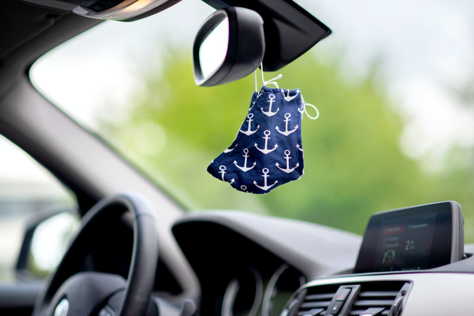 Eine blaue Stoffmaske mit Anker-Motiv hängt an einem Rückspiegel in einem Auto.